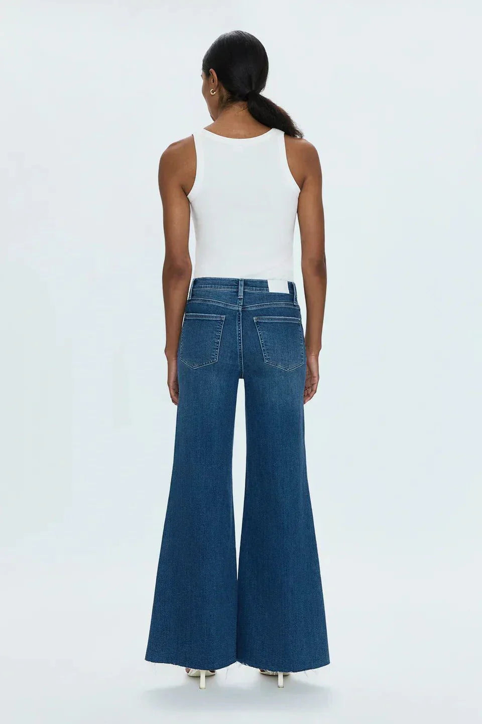 Back view of a woman wearing high-rise Izzy Jeans with a flared leg and white tank top