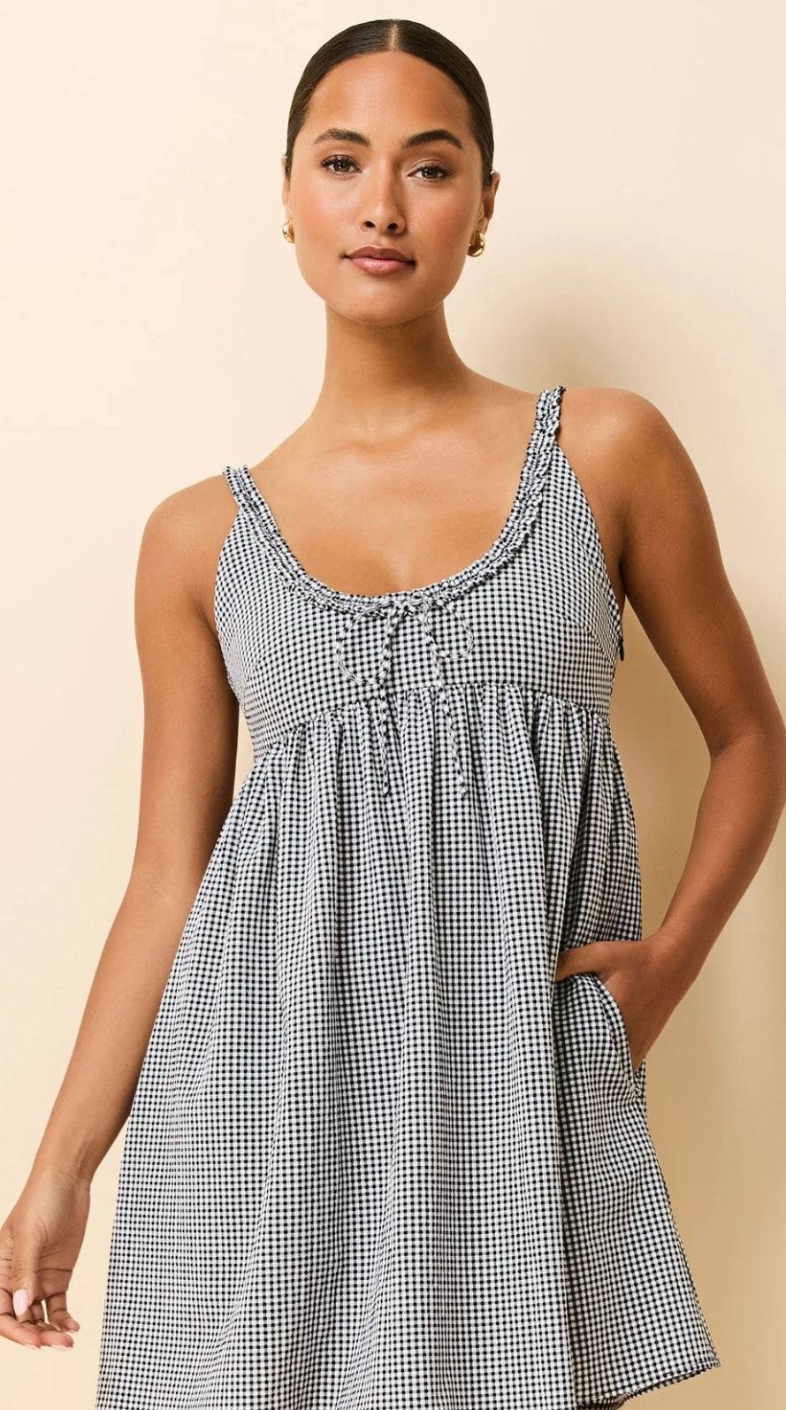 Woman wearing The Cassidy Noir gingham baby doll dress with ruffled neckline and bow tie detail