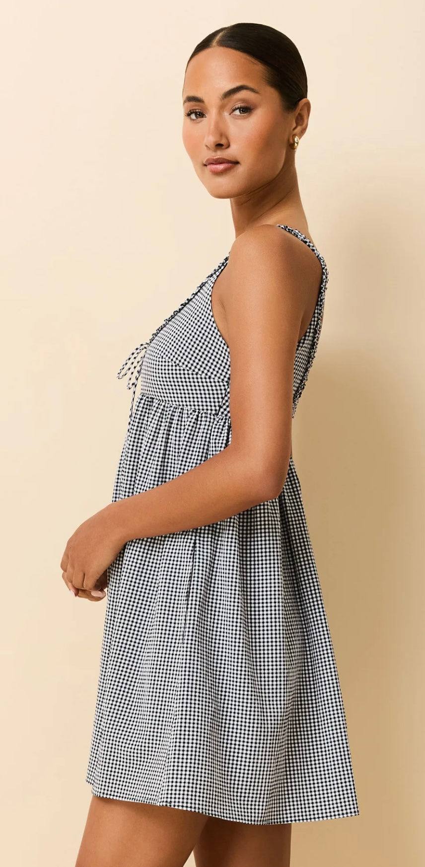 Woman wearing The Cassidy Noir gingham baby doll dress with raffled neckline and bow tie detail