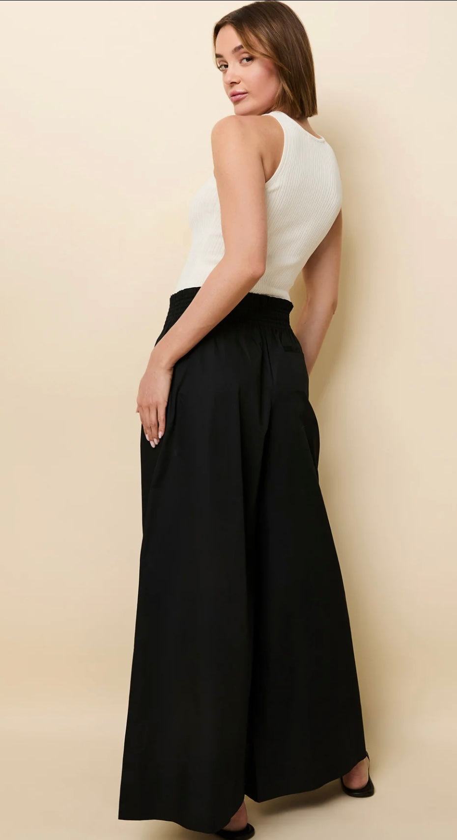 Woman wearing high-waisted black Twyla Pant Noir palazzo pants with white sleeveless top