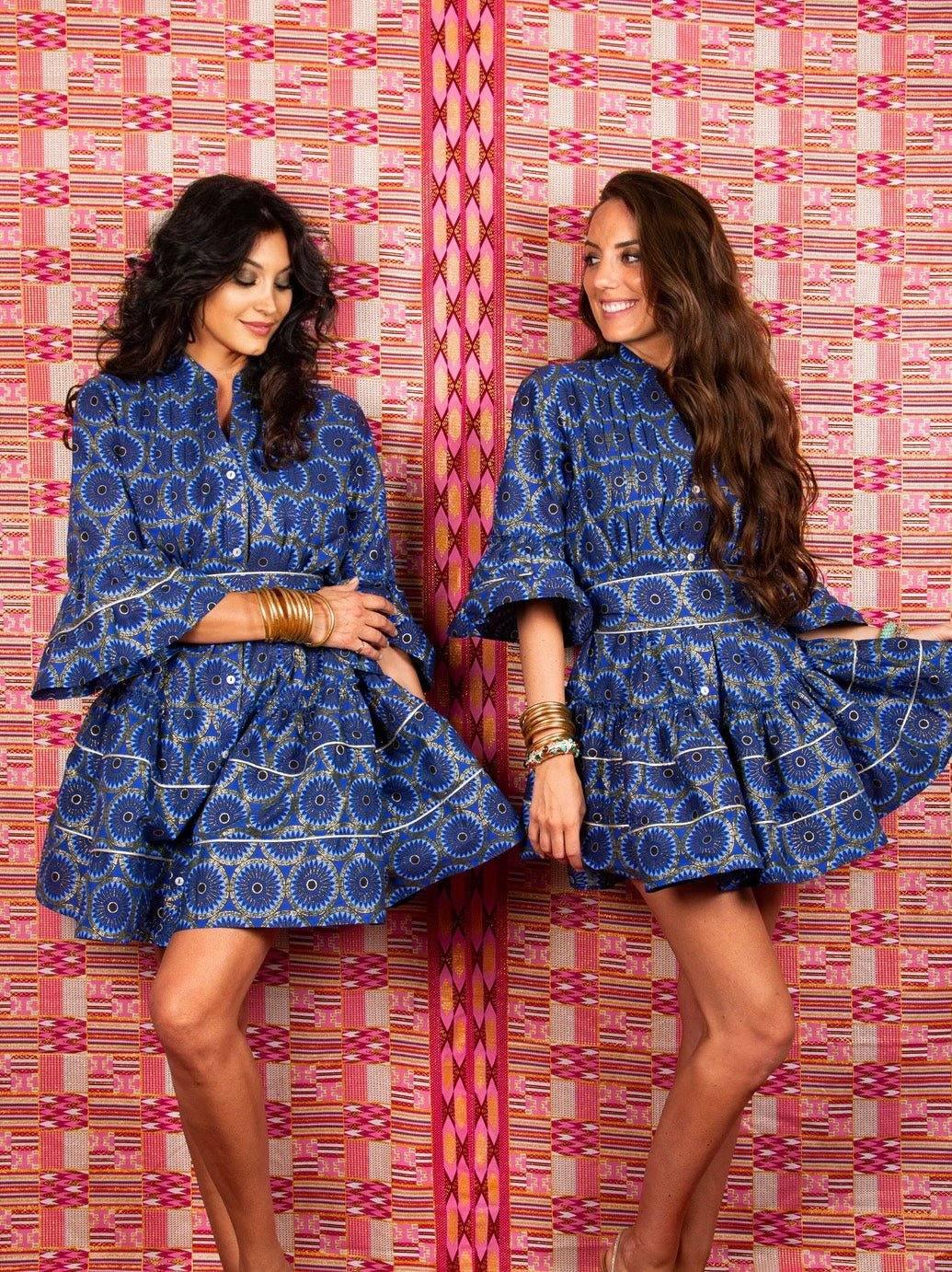 Two women wearing blue patterned Boubou dress with 3/4 sleeves and flared skirts against a colorful background