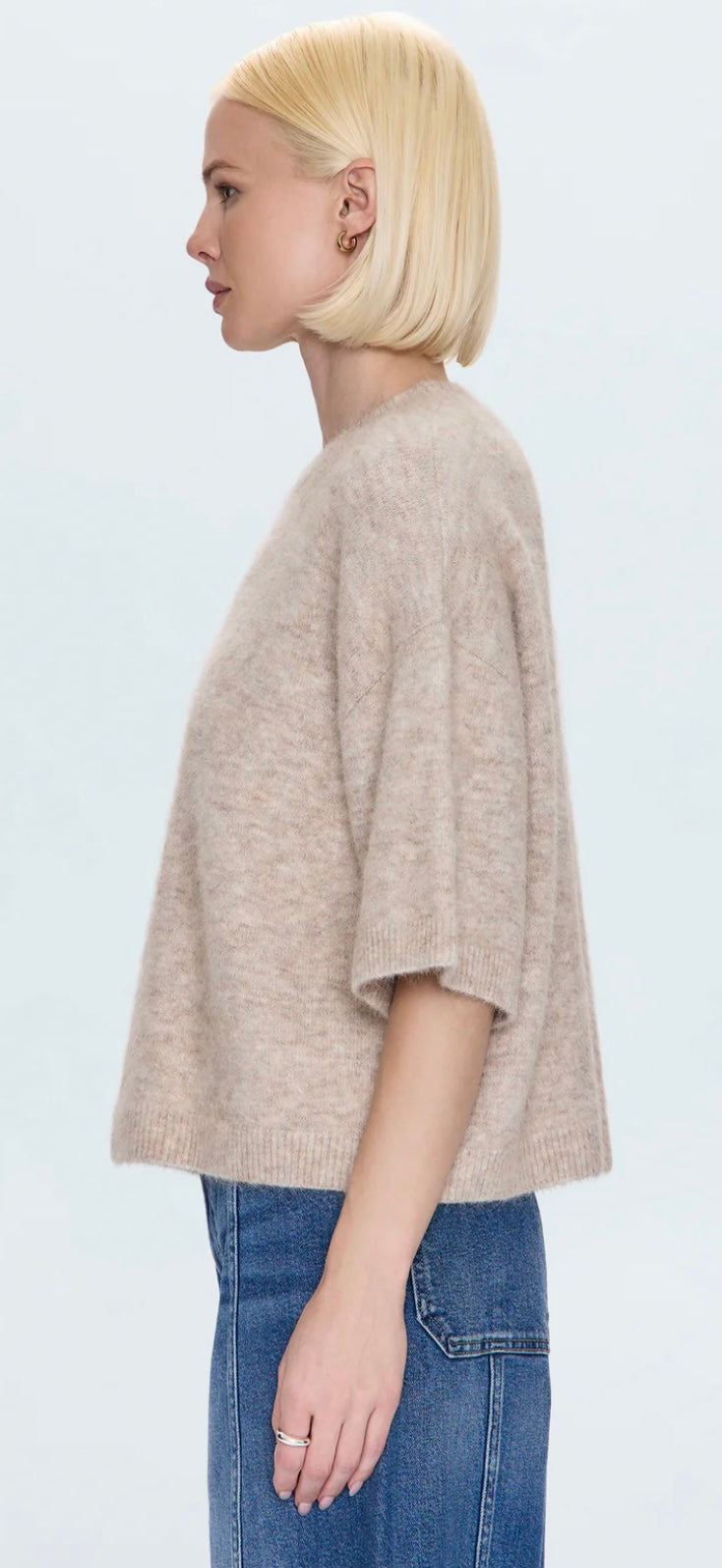 Side view of a woman wearing an oatmeal Shiloh Sweater with short sleeves paired with blue jeans