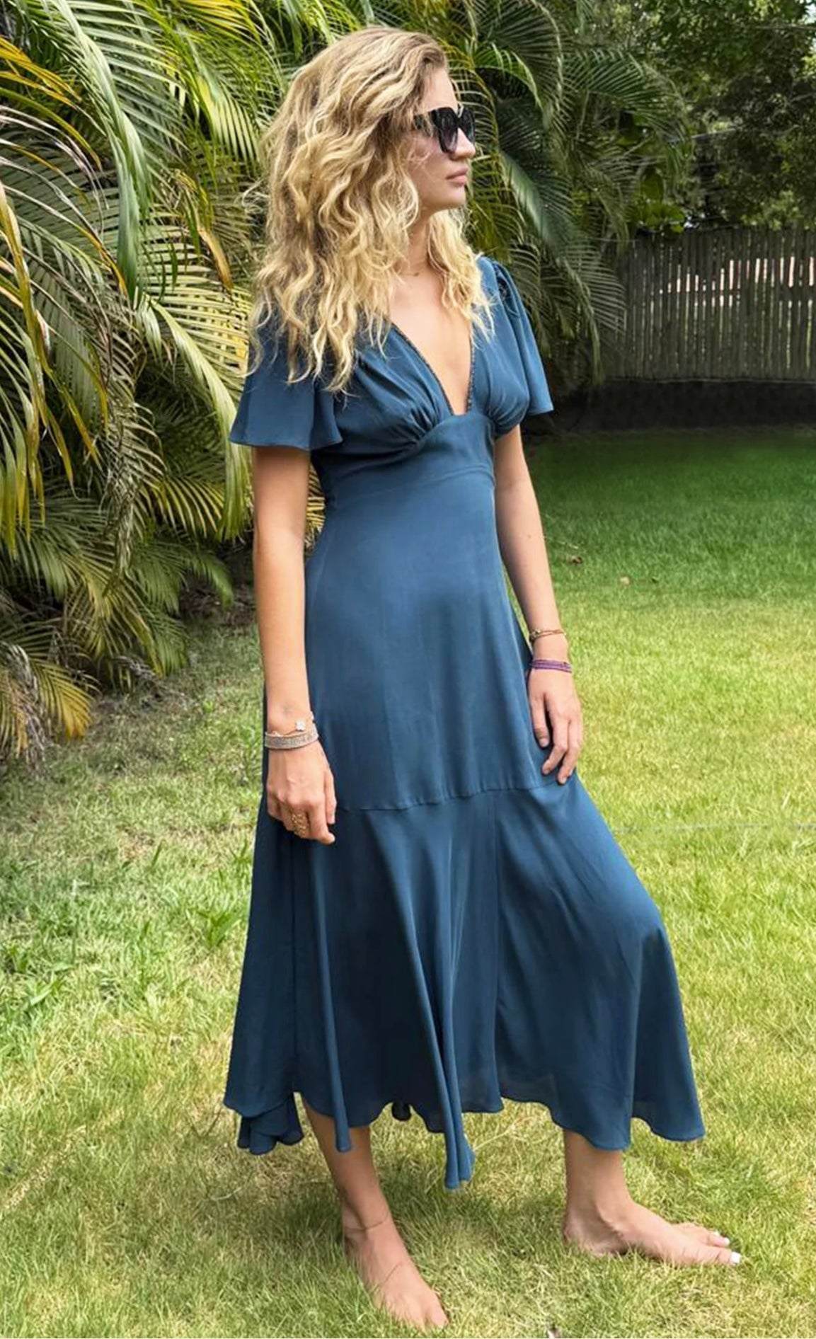 Woman wearing Iris Blue Bay Block Silk Dress standing barefoot on grass near tropical plants