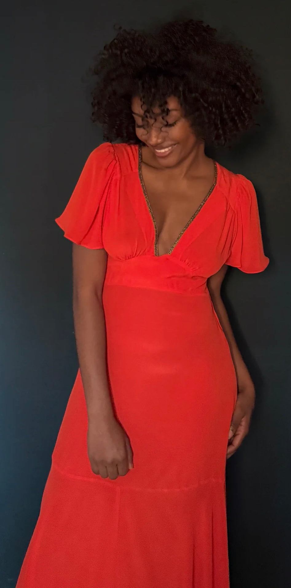 Woman wearing The Iris Fire Red dress by HANSINE LONDON with flutter sleeves and deep V neckline
