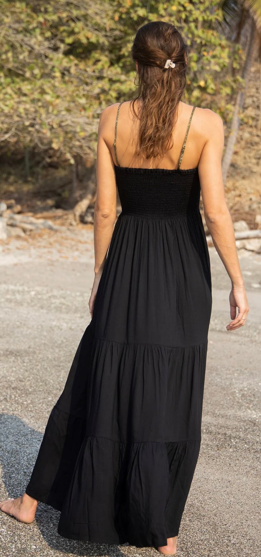 Back view of a woman wearing Gaia Dress Pure Black by HANSINE LONDON with adjustable straps and tiered ruffles outdoors