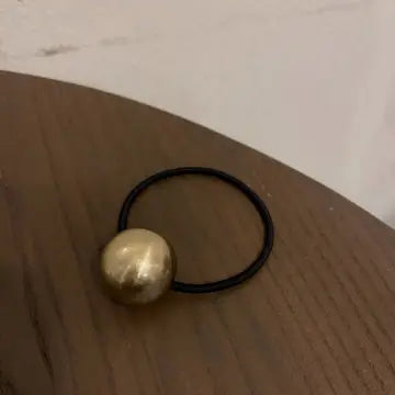 Black hair tie with gold decorative bead on wooden surface