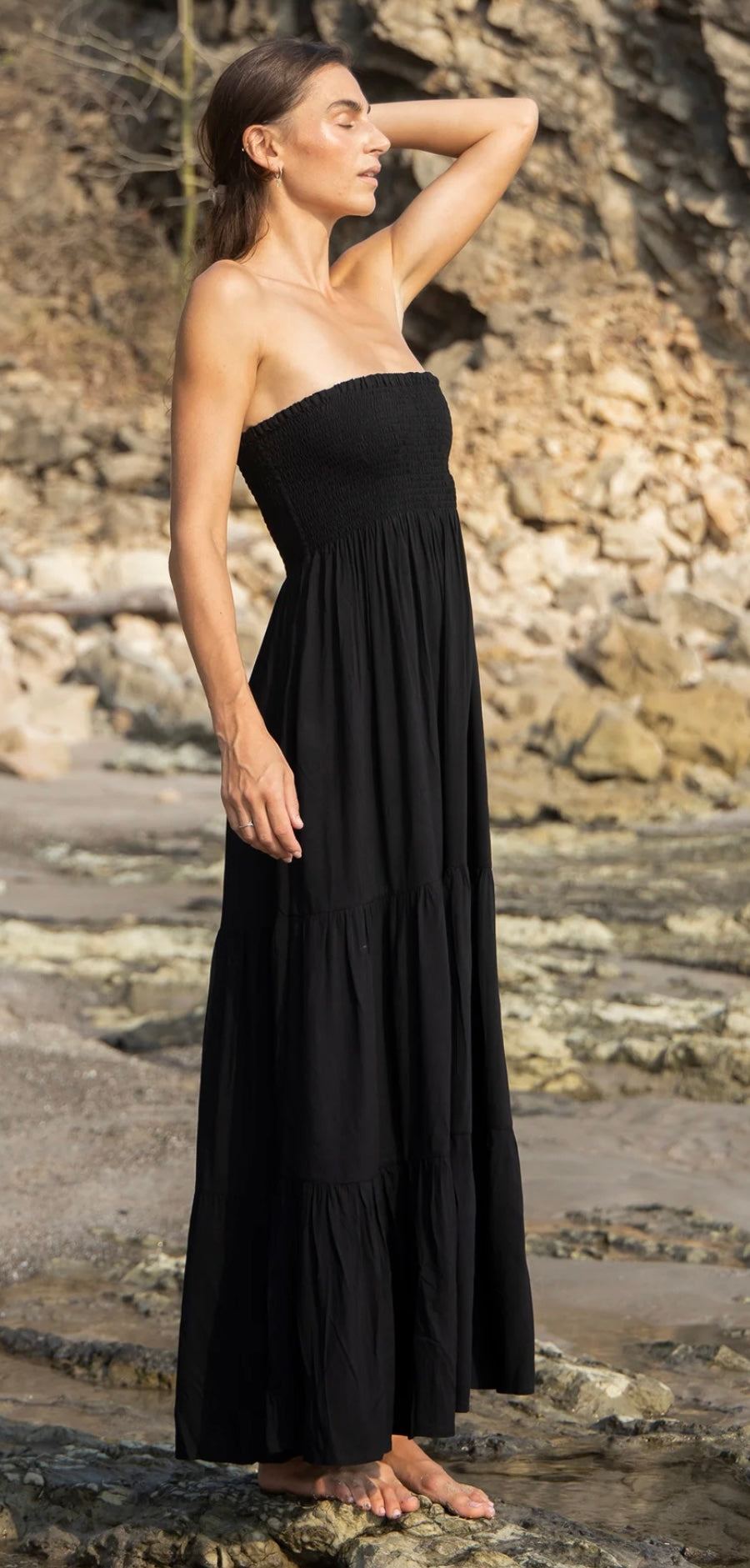 Woman wearing a black Gaia Dress by HANSINE LONDON with tiered ruffles and a bandeau top at the beach
