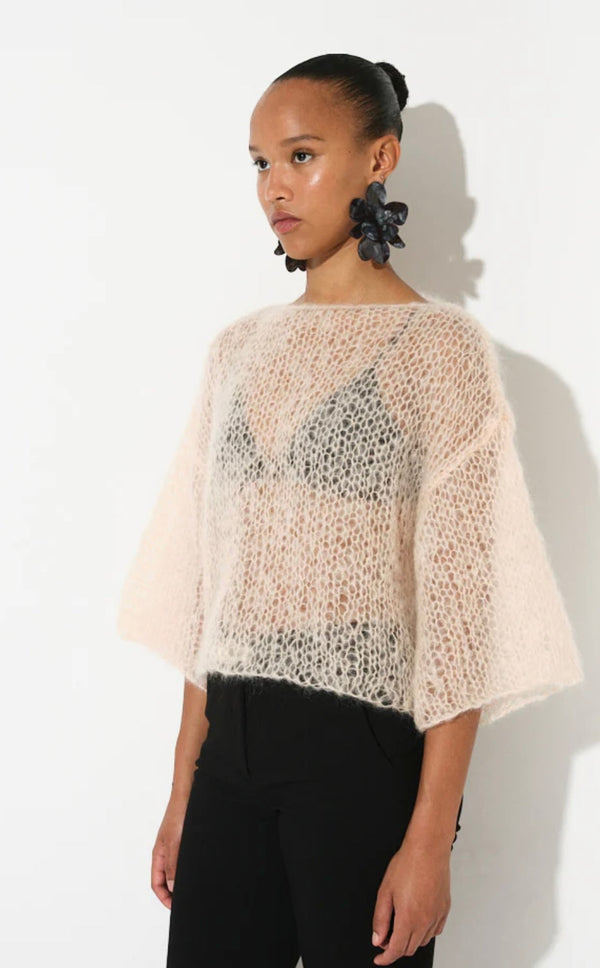 Woman wearing a sheer butter-colored mohair t-shirt with wide sleeves and black pants