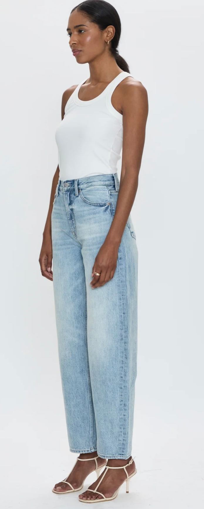 Woman wearing Wes High Rise barrel jeans in light blue denim with white tank top and heels