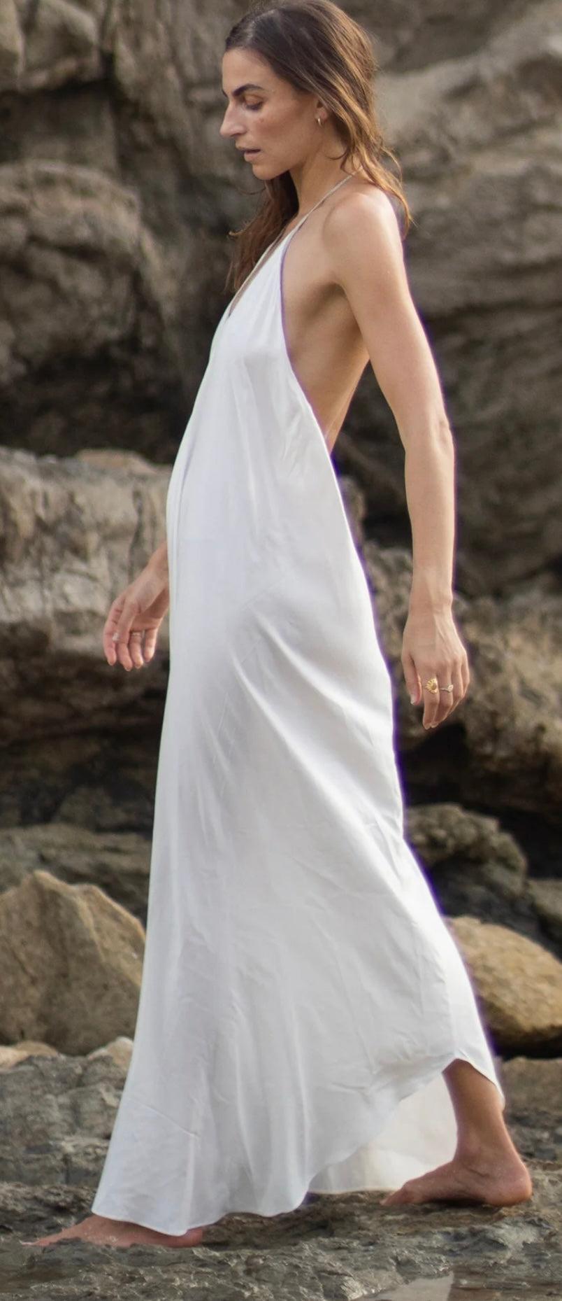 Woman wearing white Rhodes Dress with low back and V-neckline on rocky beach
