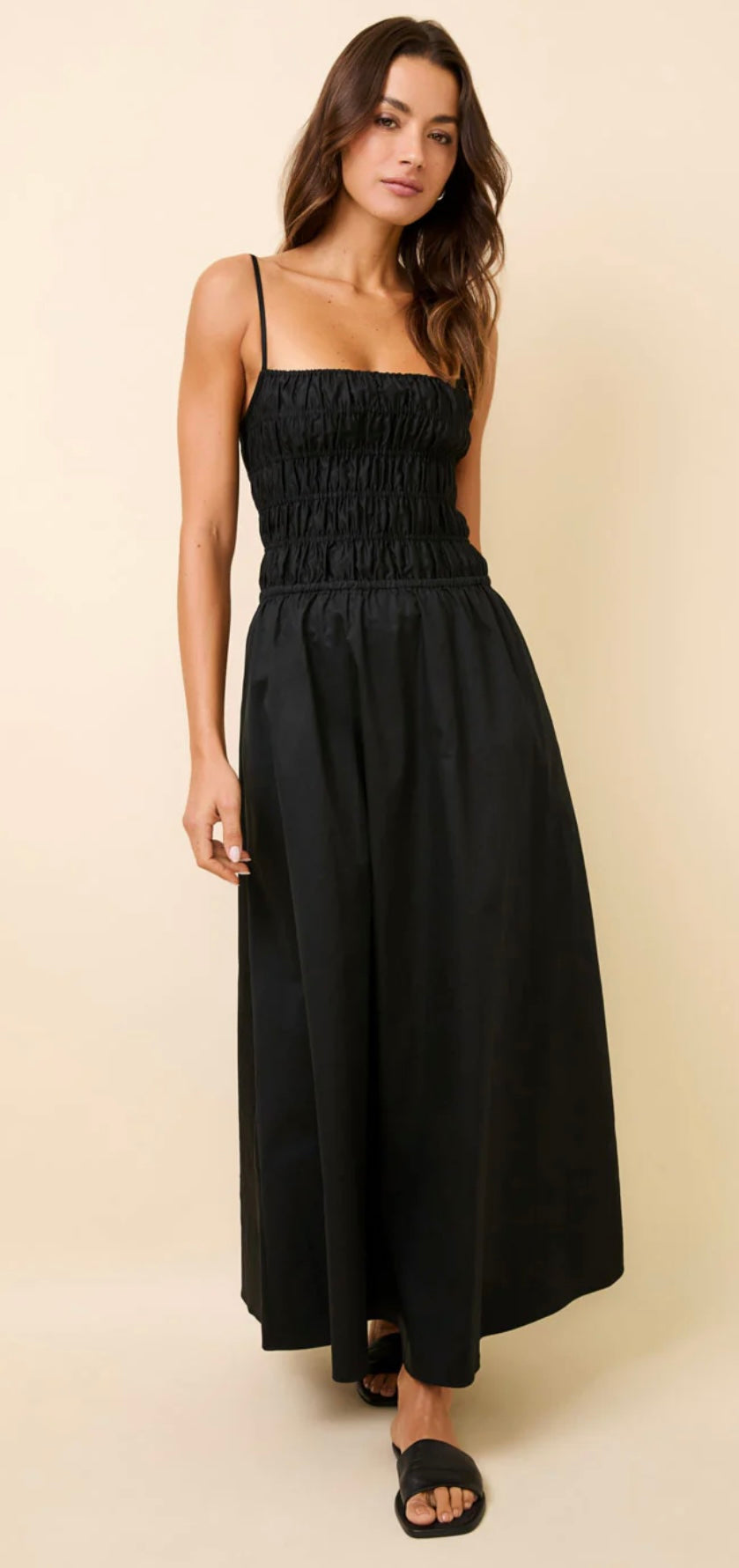 Woman wearing black Delta Dress midi with smocked bodice, adjustable straps, and relaxed skirt with pockets