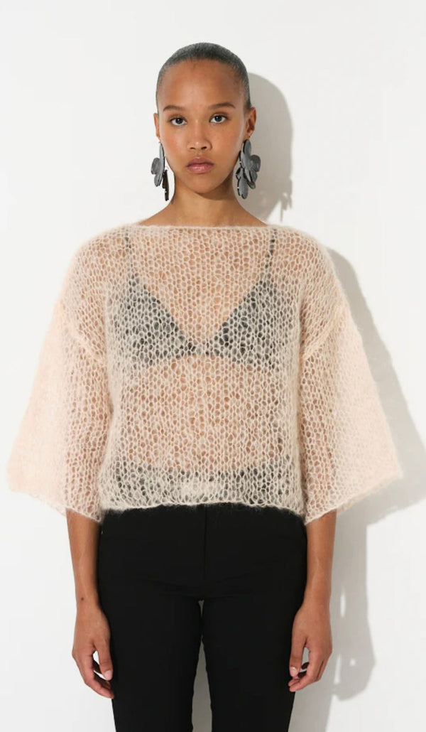 Woman wearing a light pink mohair t-shirt with wide sleeves and black pants