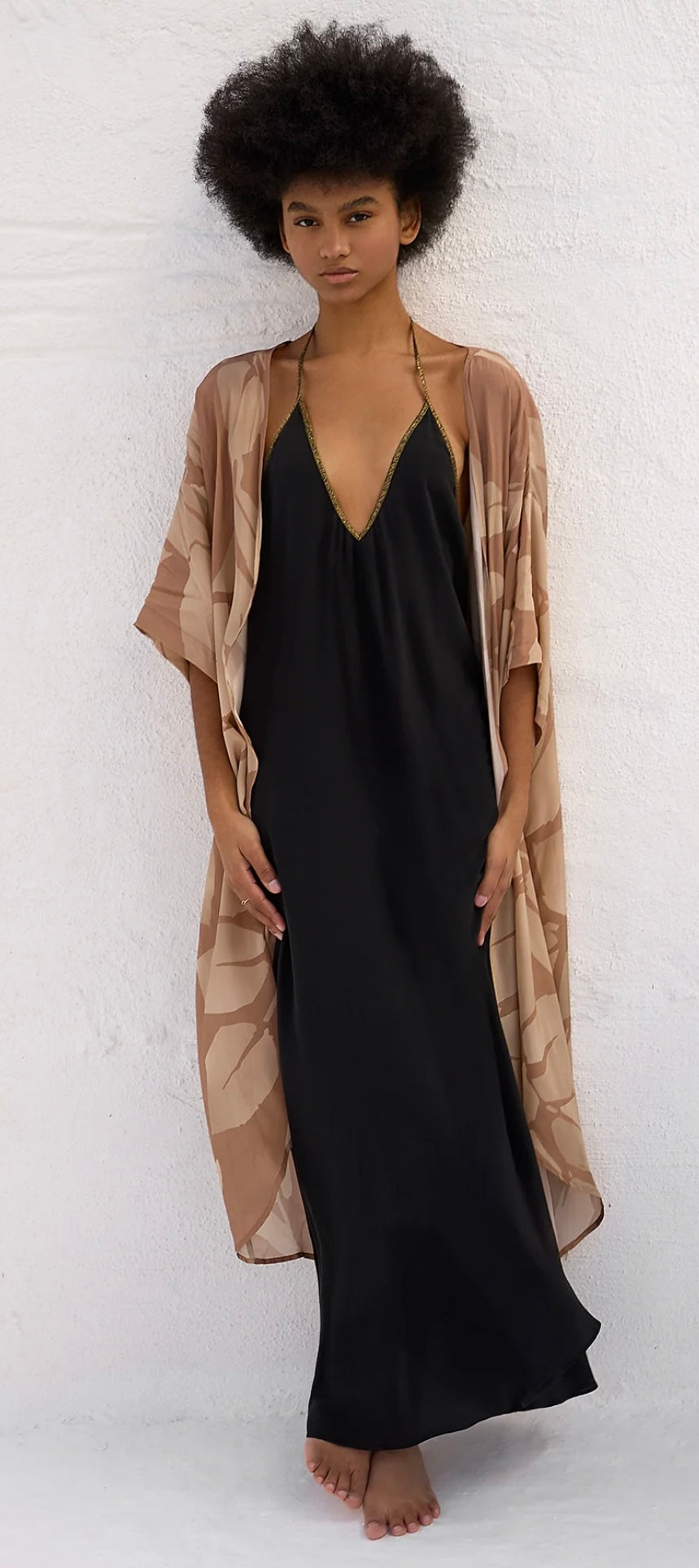Model wearing Rhodes Dress in pure black with a high-low hemline and a beige patterned overcoat.