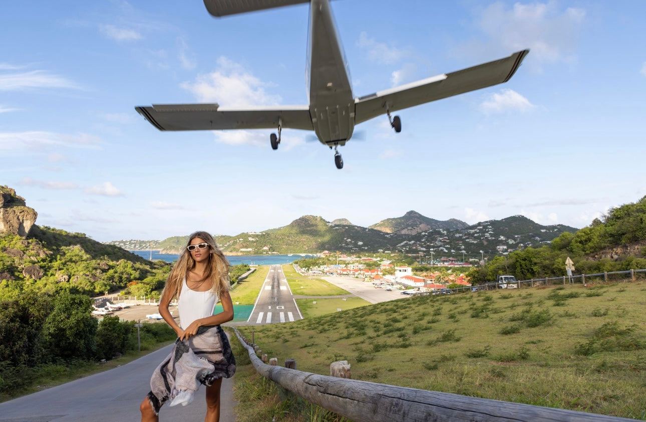Cashmere St Barth Landing scarf worn by woman near airport runway with plane overhead and scenic island background
