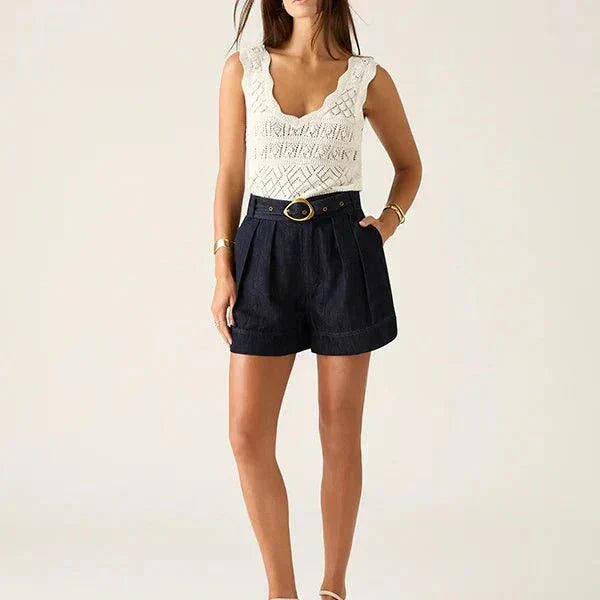 Woman wearing Ana Denim Shorts in indigo with a white sleeveless top and gold belt detail
