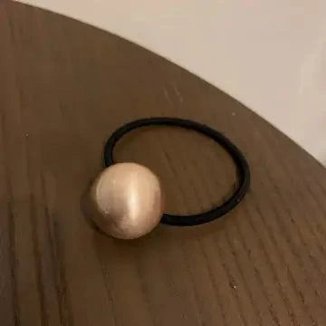 Black hair tie ponytail holder with large gold bead accessory on wooden surface