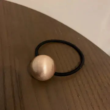 Black hair tie ponytail holder with large gold bead accessory on wooden surface