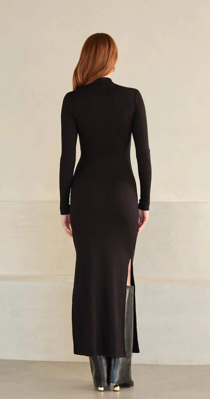Back view of a woman wearing a black Mock Neck Lux Rib Dress with long sleeves and side slit.