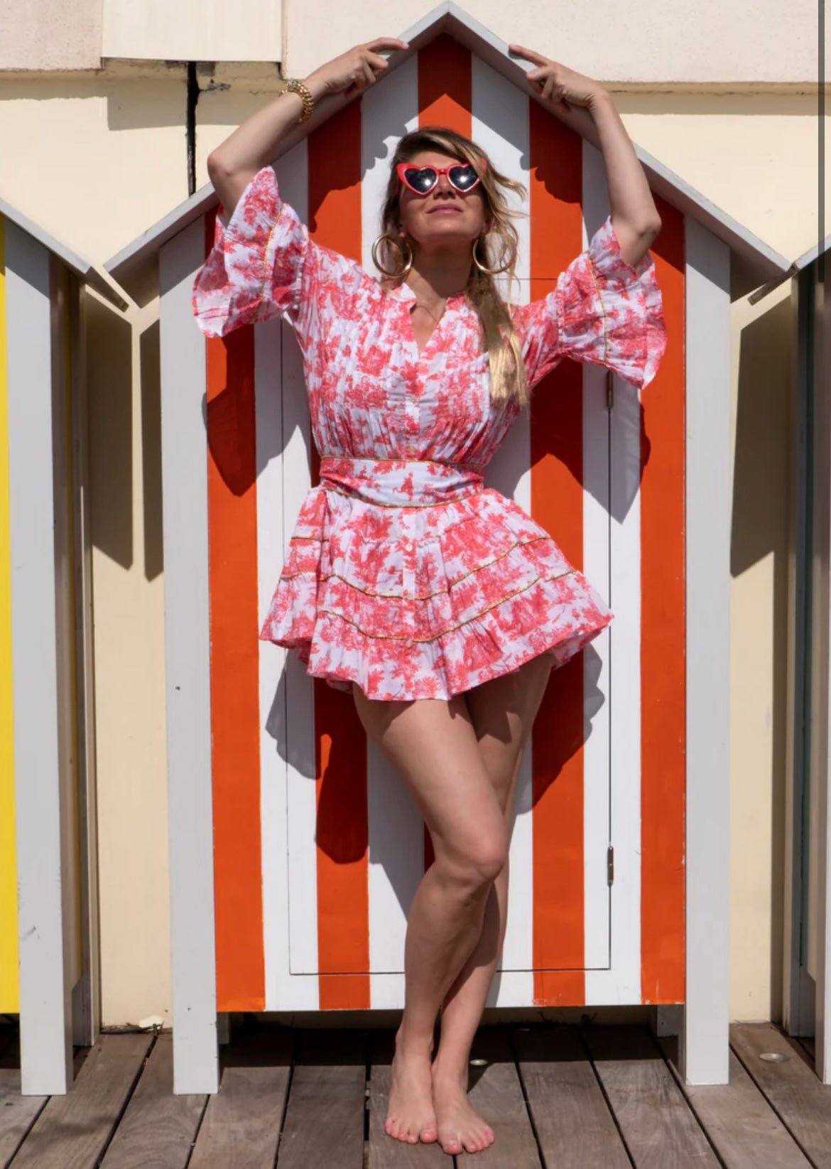 Woman wearing The Monte Carlo floral dress posing in front of striped beach hut
