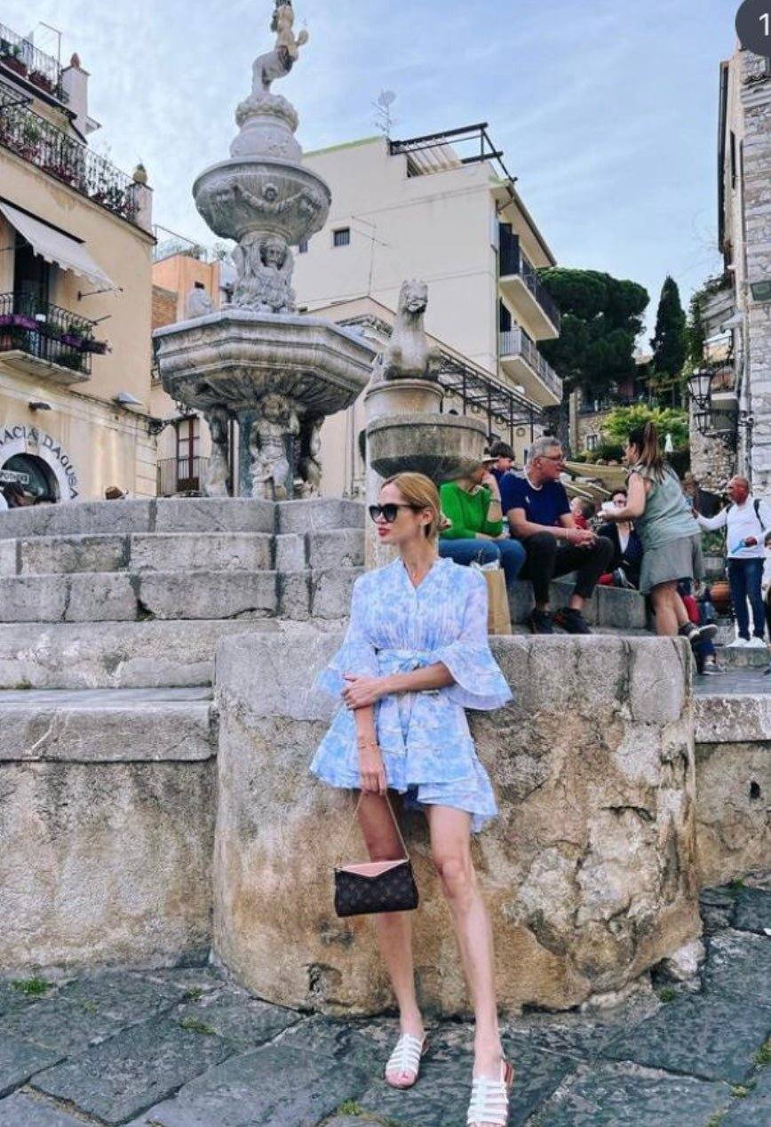 Woman wearing The Monte Carlo limited edition dress stands by historic stone fountain in scenic European town square