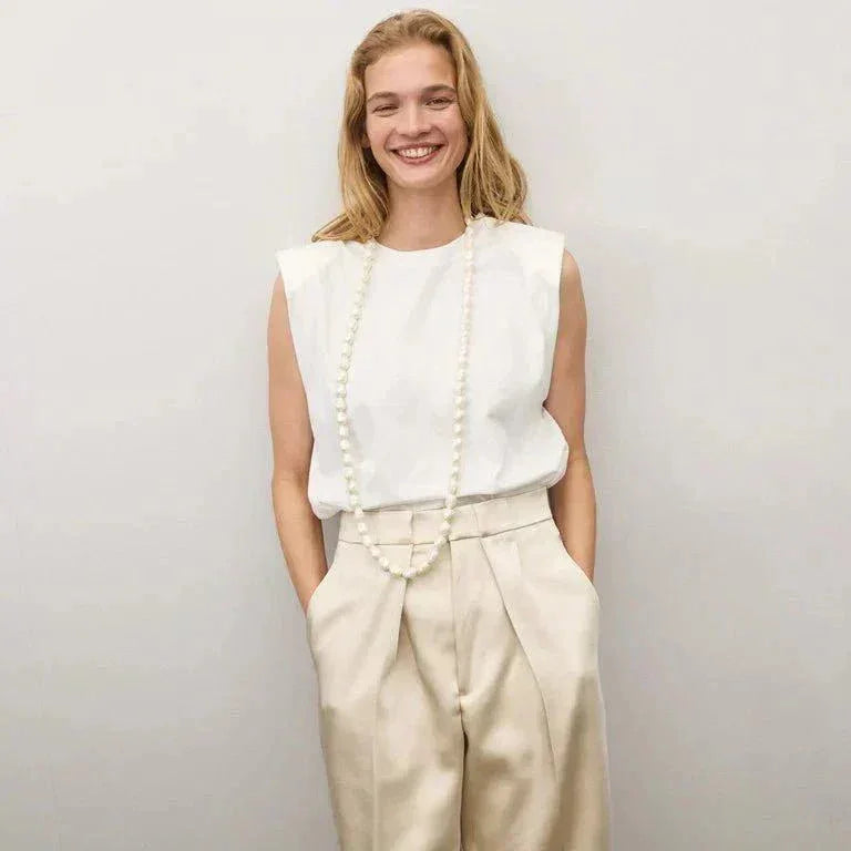 Woman wearing Organic Pearl Long Necklace by Vanessa Baroni with white sleeveless top and beige pants